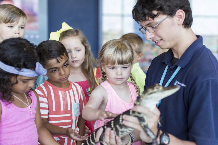 a group of children surround a South Carolina Aquarium educator holding a baby American alligator