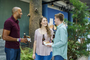 Two men and a woman talk in front of a South Carolina Aquarium exhibit. They have beer and food in their hands.