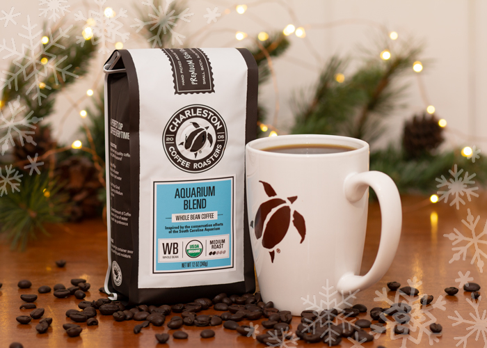 A bag of Charleston Coffee Roasters Aquarium Blend sits next to a coffee mug with a sea turtle on it in front of holiday lights.