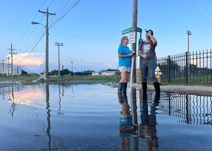 A South Carolina Aquarium employee in an aqua shirt, khaki shorts and rainboots assists a Southern Environmental Law Center employee in a gray shirt, blue pants and rain boots in tracking flooding on Charleston streets
